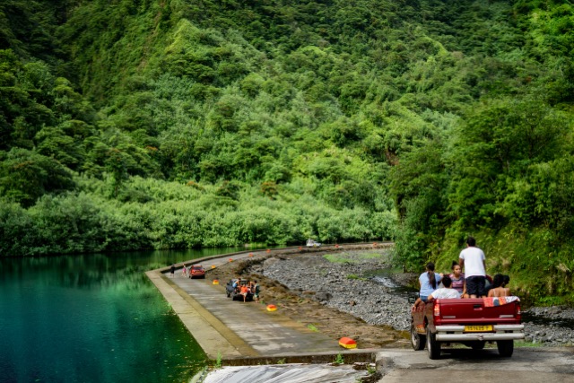 A truck with tourists in the back driving through tropical hills next to a lake